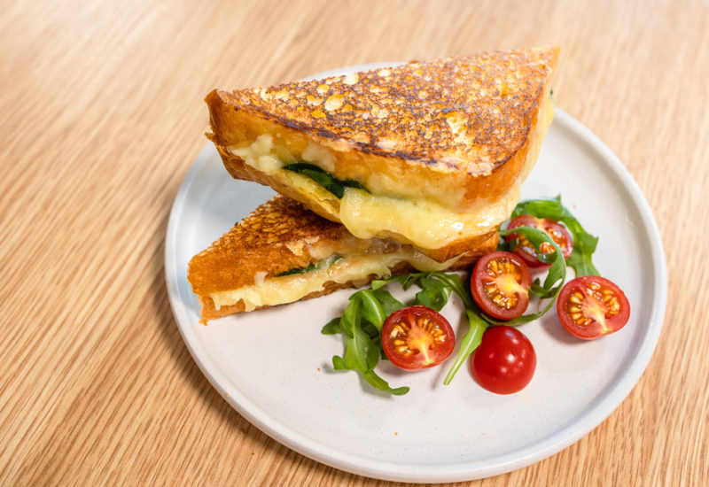Brioche Grilled Cheese Sandwich Header Photo A Brioche Grilled Cheese Sandwich recipe on a white plate next to lettuce and tomatoes