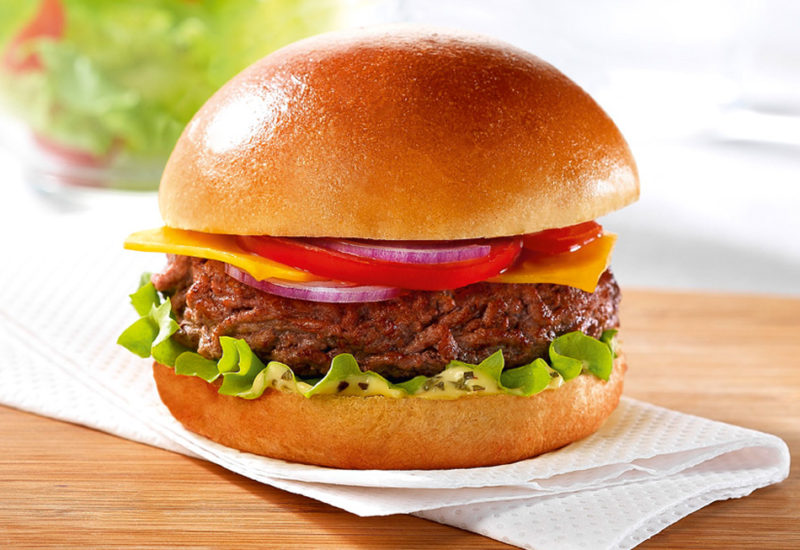 A Classic Brioche Cheeseburger recipe on top of kitchen roll on a wooden board